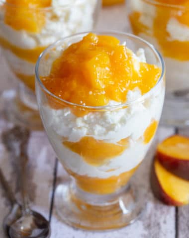 3 glasses of mousse on a white board with spoons and 2 slices of peaches
