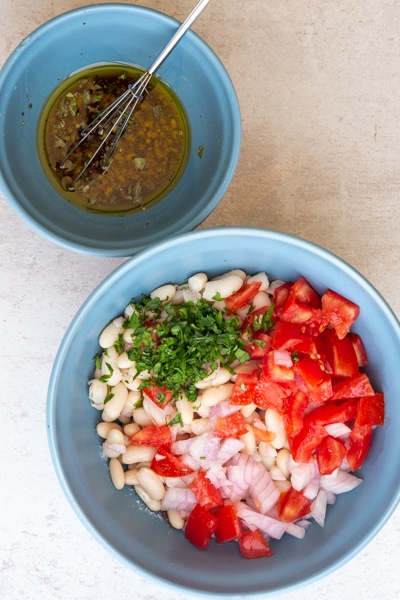 dressing in a blue bowl and bean salad ingredients in a bigger blue bowl