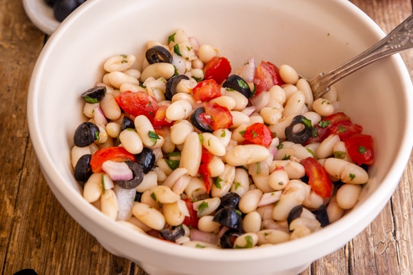 bean salad in a white bowl with a silver spoon