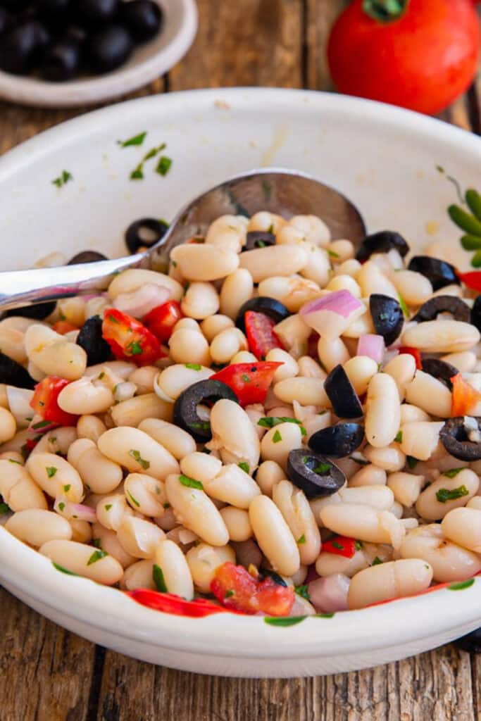 Bean salad in a white bowl with a spoon.