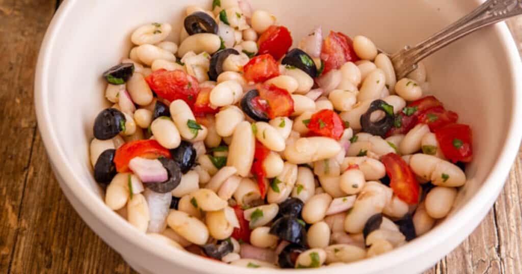 Bean salad in a white bowl with a spoon.