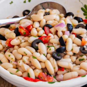 Bean salad in a white bowl with a spoon.