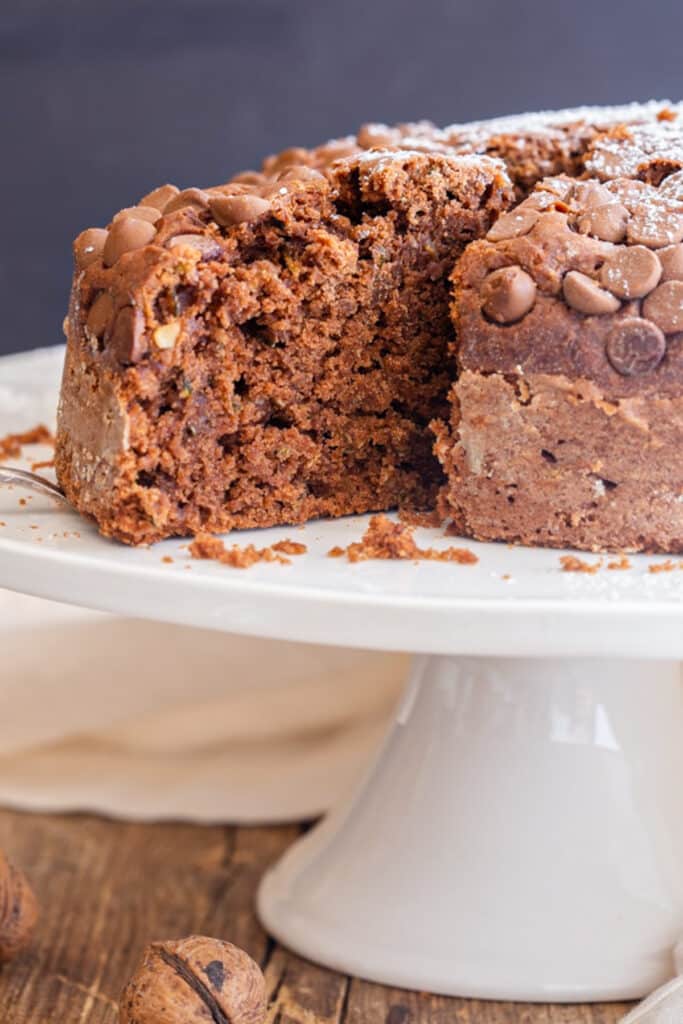 Zucchini cake on a white cake stand with a slice cut.