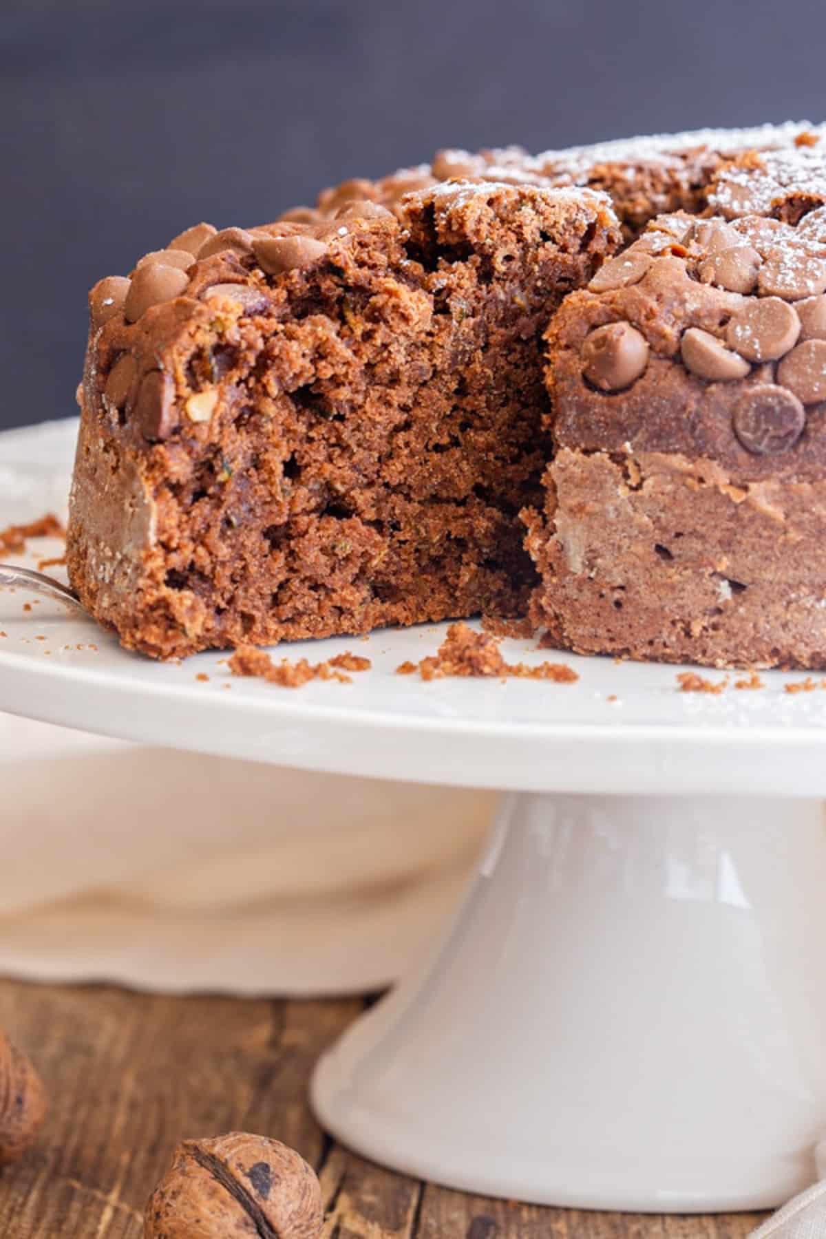 Zucchini cake on a white cake stand with a slice cut.