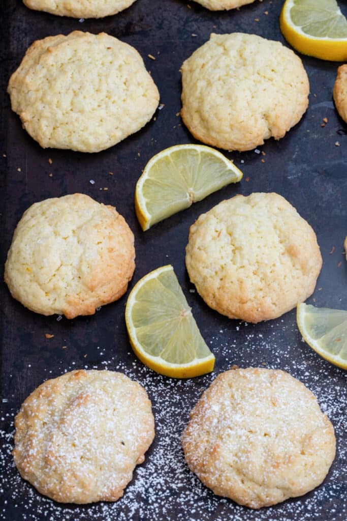 Lemon cookies on a black cookie sheet with slices of lemon.