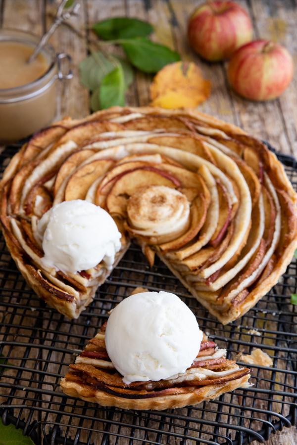 puff pastry apple pie on a black cake rack with a cut sliced and a scoop of ice cream on top