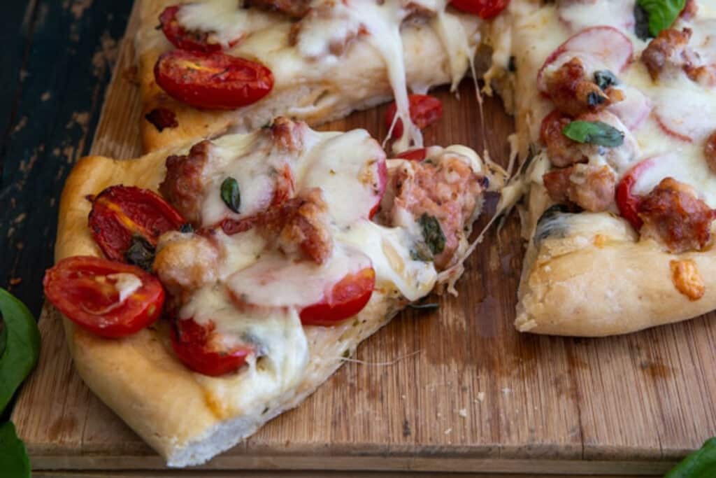 Pizza on a wooden board with a slice cut.