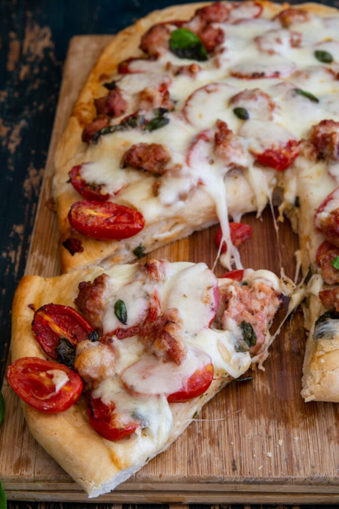 Pizza on a wooden board with a slice cut.