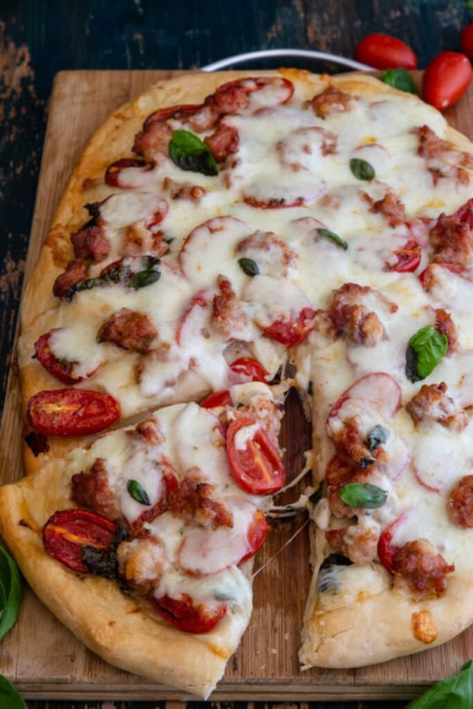 Pizza on a wooden board with a slice cut.