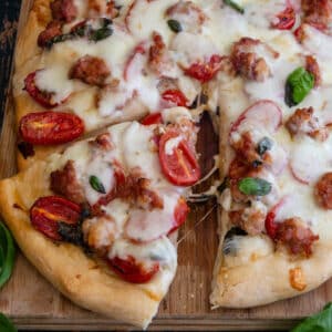 Pizza on a wooden board with a slice cut.