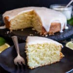 The lemon cake on a cake stand with a slice on a black plate.