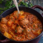 meatball stew in a red pot with a silver spoon
