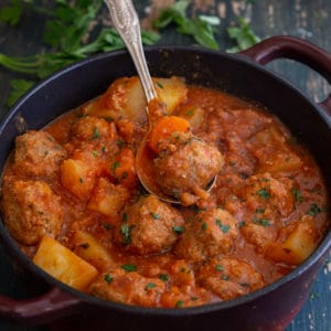 meatball stew in a red pot with a silver spoon