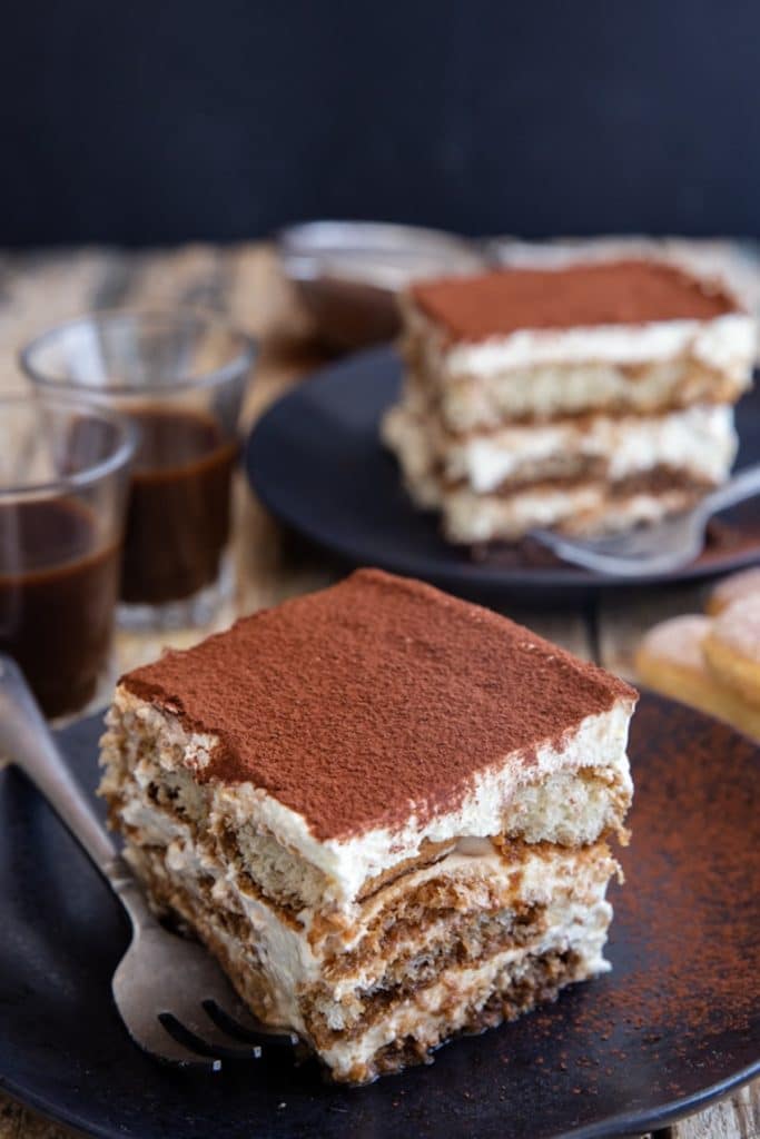 Two slices of tiramisu on black plates.