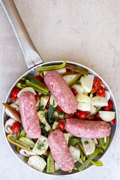 adding the vegetables and sausages in a silver frying pan