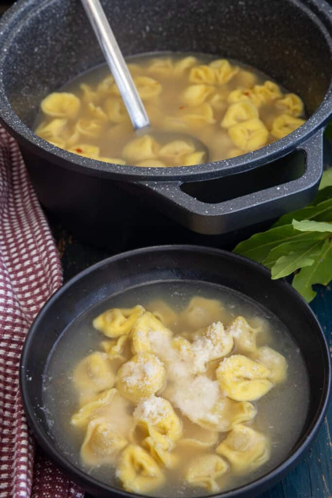 Tortellini in brodo in a black pot and in a black bowl.