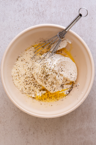 egg, ricotta, parmesan and spices in a white bowl with a whisk