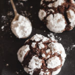 crinkle cookies on a black board with a spoon of powdered sugar