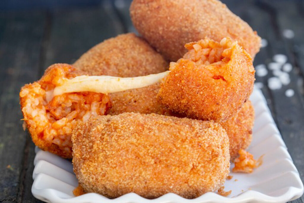 Italian rice balls on a white dish with one broken in half.