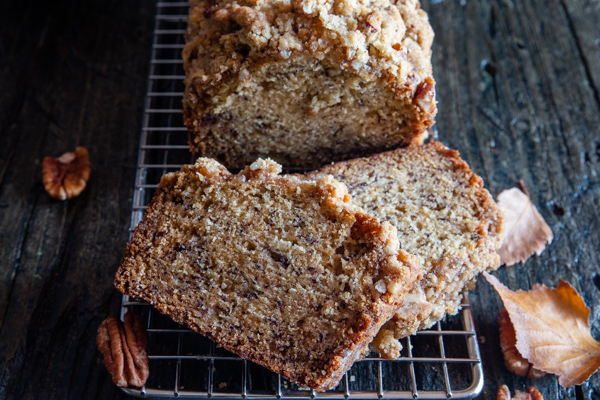 banana bread on a wire rack with 2 slices cut.