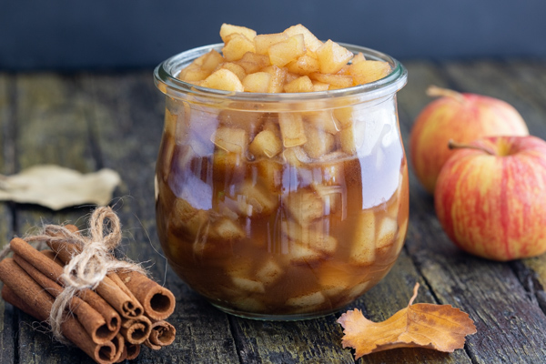 caramelized apples in a jar with cinnamon sticks and 2 apples