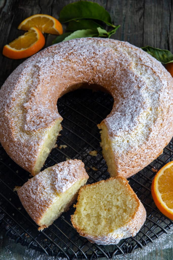Orange cake with two slices cut on a black wire rack.