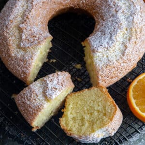 Orange cake with two slices cut on a black wire rack.
