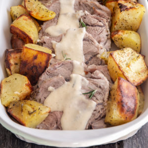 sliced beef with sauce and potatoes in a white pan