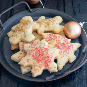 sugar cookies on a black plate with fairy lights and Christmas tree balls