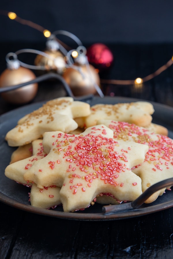 sugar cookies on a black plate with fairy lights and Christmas tree balls