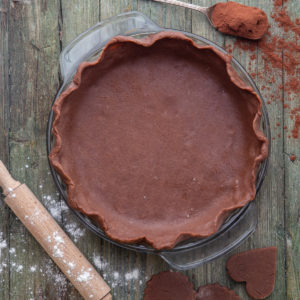 pastry dough in a pie plate with a spoon of cocoa & rolling pin