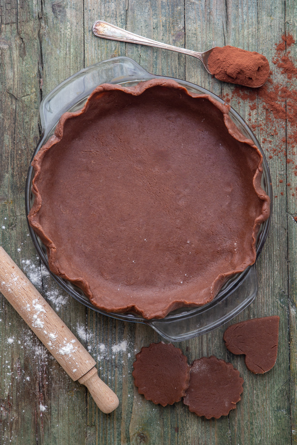 pastry dough in a pie plate with a spoon of cocoa & rolling pin