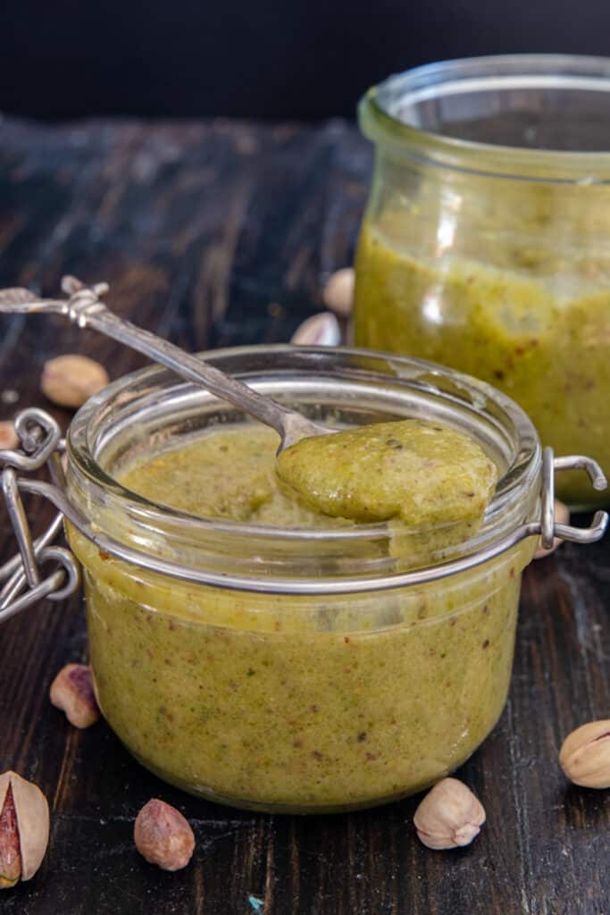 Pistachio cream in a glass jar and some on a spoon.