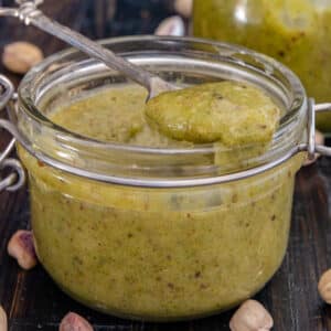 Pistachio cream in a glass jar and some on a spoon.