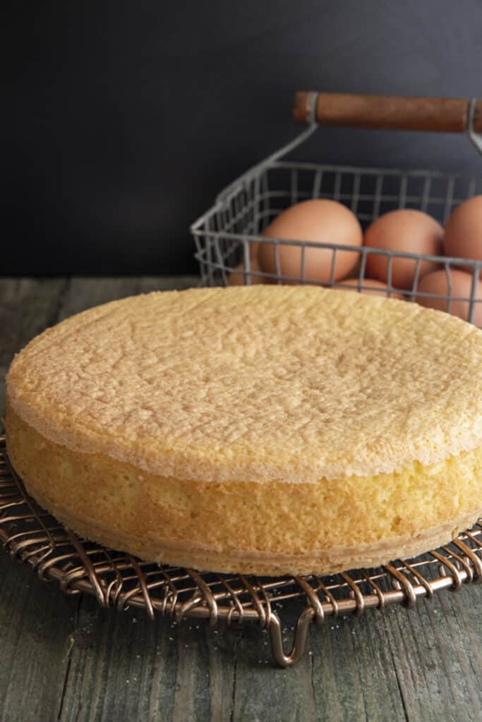 Sponge cake on a wire rack with eggs in a basket.