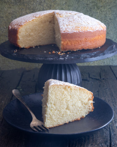 cake on a stand with a slice on a black plate with a silver fork