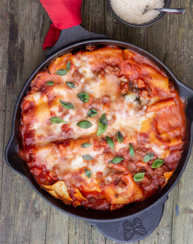 lasagna in the skillet with a small bowl of parmesan cheese and a spoon