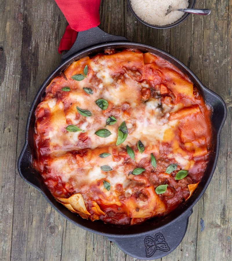 lasagna in the skillet with a small bowl of parmesan cheese and a spoon