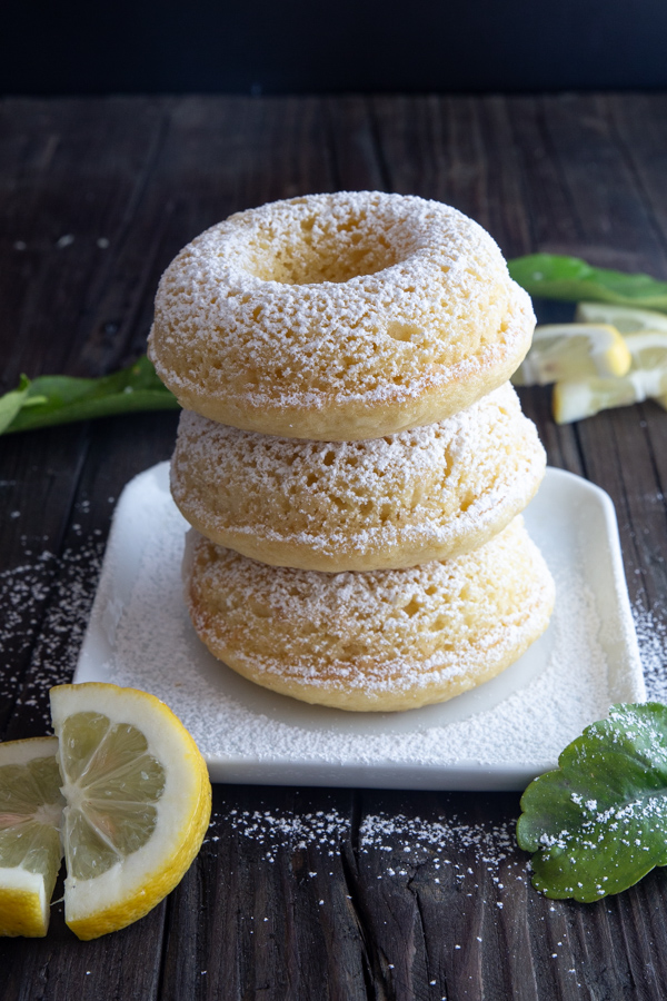 3 lemon donuts dusted with powdered sugar stacked on a white square plate