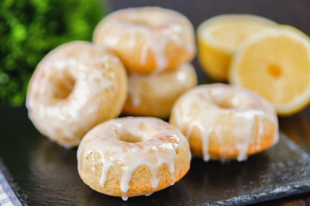 Five glazed donuts on a black plate.