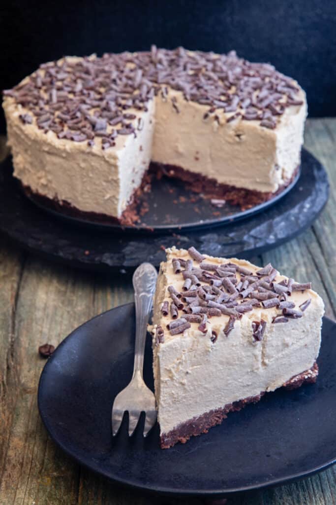 Coffee cheesecake on a black stand with a slice on a black plate.