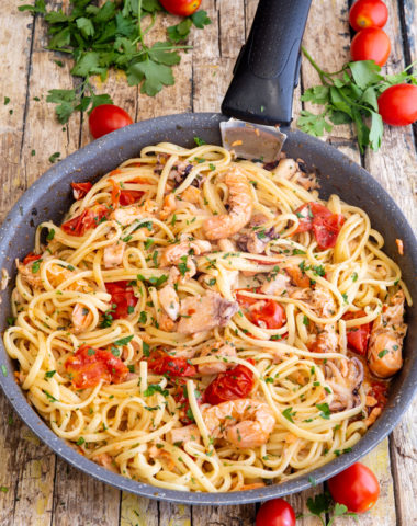 seafood pasta in a black pan, with grape tomatoes around it.