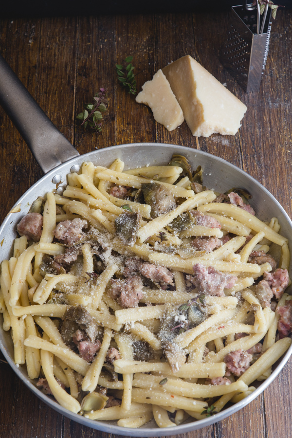 sausage & artichoke pasta in a silver pan sprinkled with parmesan cheese.