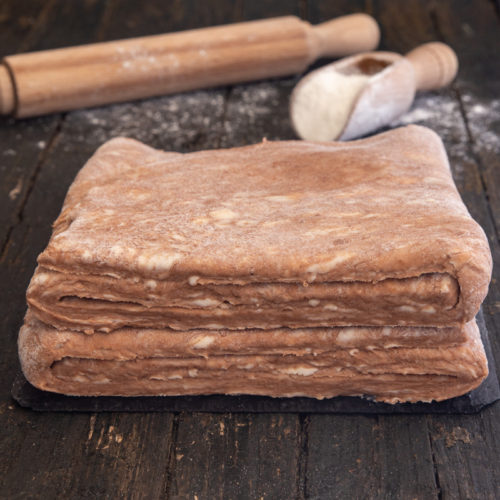 puff pastry with a rolling pin and small scoop of flour on a brown board.