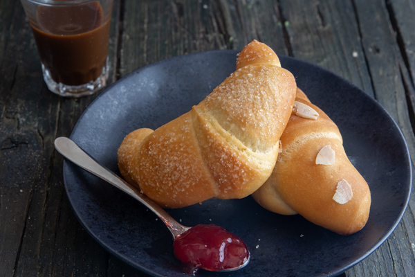2 crescent rolls on a black plate with a spoonful of jam.
