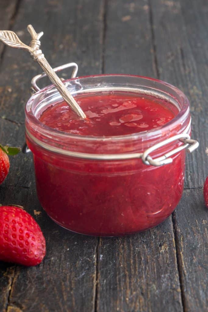 Strawberry jam in a glass jar with a spoon.