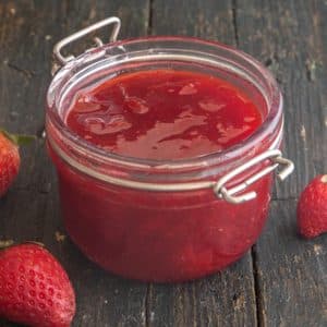 Strawberry jam in a glass jar with a spoon.