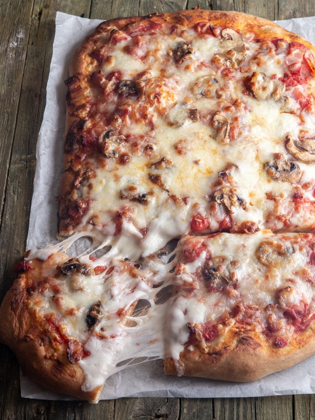 pizza on parchment paper with a slice cut.