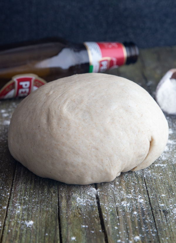 Beer pizza dough on a board with a bottle of beer behind it.