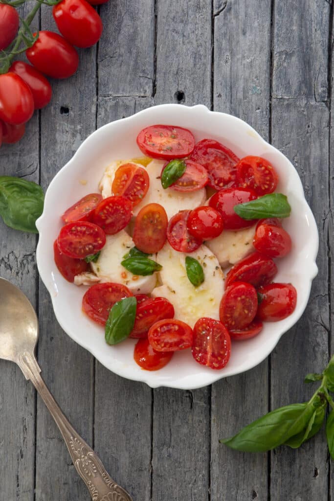 Caprese in a white dish with tomatoes and a spoon.